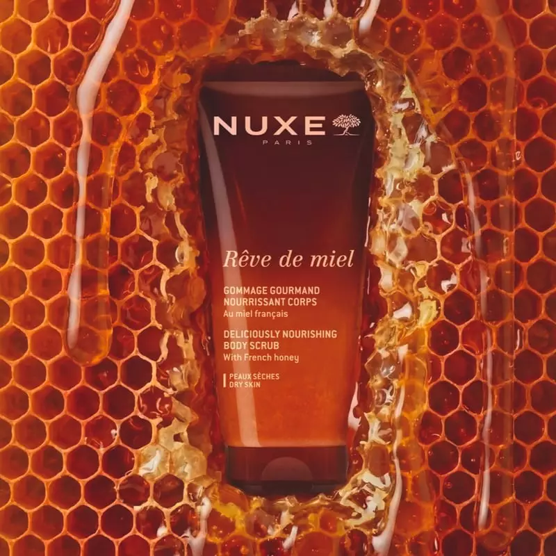 Tube de gommage corps Nuxe Rêve de Miel entouré de rayon de miel doré et de miel coulant, mettant en