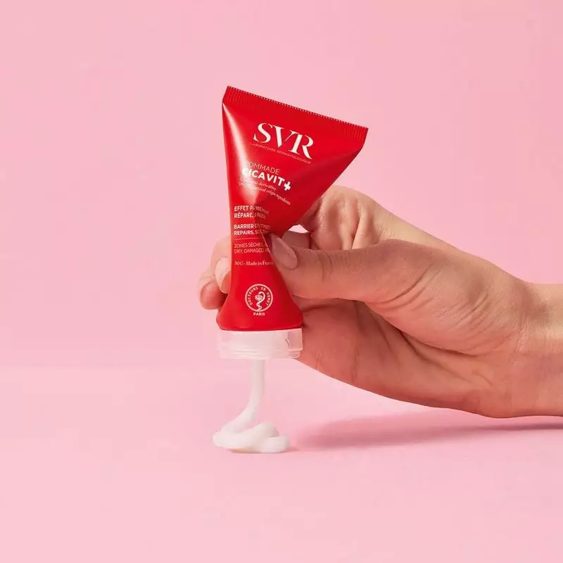 Main pressant le tube SVR Cicavit+ Pommade réparatrice 50 g, baume blanc épais s’écoulant sur fond r
