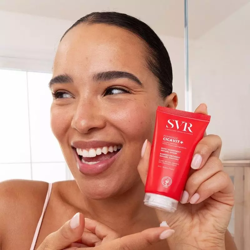Femme souriante tenant le tube rouge SVR Cicavit+ Pommade réparatrice 50 g près de son visage dans u